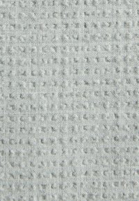 Tejido gris claro con un patrón texturizado de pequeños cuadrados, creando una variación de superficie única. Material suave y tejido con una profundidad sutil.