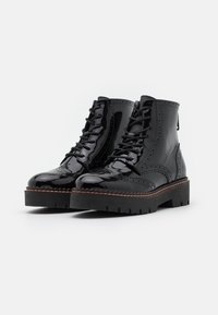 Black patent leather ankle boots with a chunky rubber sole, lace-up design, brogue detailing, and a smooth finish.