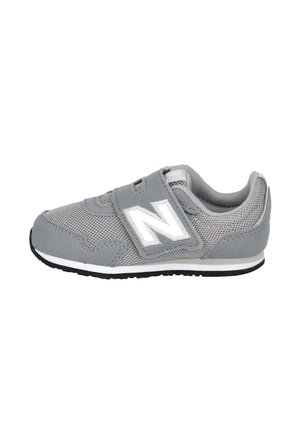 Zapatilla deportiva infantil gris con logo blanco "N", parte superior de malla y cierre de velcro, suela negra y blanca, vista lateral sobre fondo blanco.