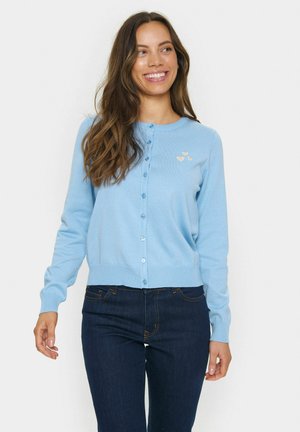 Cardigan bleu clair en matière tricot douce, avec un col rond, une fermeture à boutons et une petite broderie en forme de cœur jaune sur le côté gauche.