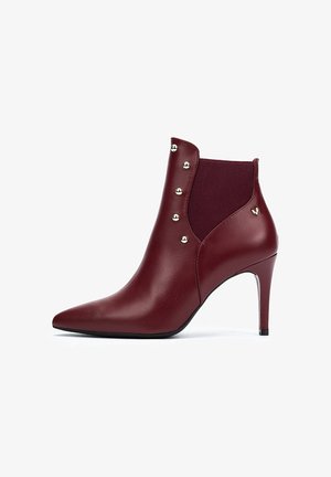 Botín de cuero burdeos con punta afilada, panel lateral elástico y tachuelas doradas decorativas a lo largo del costado, que presenta un tacón delgado.