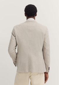 Hellgraue Sakkojacke mit glatter Textur, strukturiertem Design und zwei Knöpfen, ausgestattet mit dunkelbraunen Knöpfen und einem taillierten Schnitt.