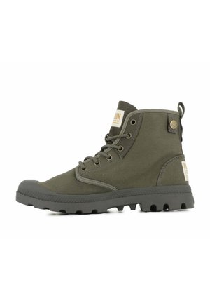 Botas hasta el tobillo en verde oliva con parte superior de lona, suela de goma y punta redonda. Presentan ojales de metal y una lengüeta en la parte posterior. Marca en el panel lateral.