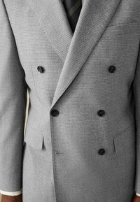 Graue, doppelt-knöpfige Sakko mit strukturiertem Muster, ausgestattet mit zwei schwarzen Knöpfen, einer Brusttasche und einem scharfen Revers-Design.