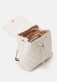 White quilted bag with a drawstring closure and gold hardware. The interior is lined in brown fabric with a zip pocket.
