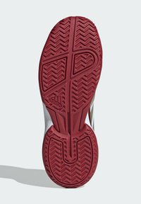 Piros gumitalpú cipő talpa, cikk-cakk mintázattal, dombornyomott logóval és dizájn vonalakkal. Az oldalak mentén sima fehér szegély látható.