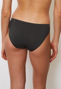 Costumi da bagno neri con una consistenza liscia e opaca. Presentano un taglio a vita bassa, un design minimalista e nessuna ferramenta o motivo visibile.