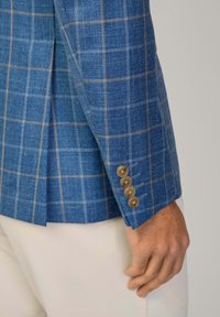Blazer a scacchi blu in tessuto testurizzato, con linee marroni chiare, quattro bottoni marroni sui polsini e una vestibilità sagomata.