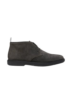 Botín de ante gris oscuro para hombre con suela negra y cordones con tres ojales, visto de lado sobre un fondo blanco.
