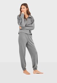 Sudadera gris con cuello de cremallera y corte holgado, combinada con pantalones de chándal gris a juego con puños elásticos, confeccionados en tela suave.