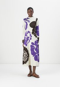 Knee-length knit dress in cream, featuring large purple and brown floral patterns, with long sleeves and a high neckline. Brown sandals.