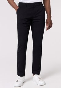 Pantaloni chino neri con vestibilità slim, dotati di tasche davanti e una piega sottile lungo la gamba, abbinati a sneakers bianche.