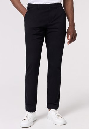 Schwarze Chinohosen mit Slim Fit, ausgestattet mit Fronttaschen und einem dezenten Bundfalten, kombiniert mit weißen Sneakern.