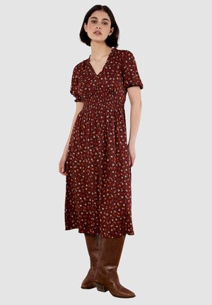 Rotes Blumenkleid mit kurzen Puffärmeln, geraffter Taille und fließendem Rock. Kombiniert mit knielangen braunen Stiefeln aus Leder.