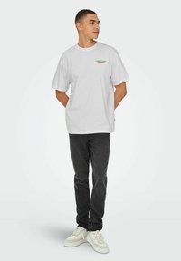 Witte katoenen t-shirt met korte mouwen met multi-gekleurde tekst "London Fields" op de linkerkant van de borst; gecombineerd met zwarte jeans en witte sneakers.