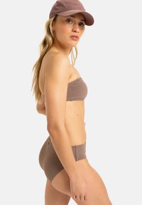 Brauner, strukturierter Bandeau-Bikini-Oberteil kombiniert mit hoch taillierten Unterteilen, die ein glattes, eng anliegendes Design zeigen. Ergänzt durch eine passende Kappe.