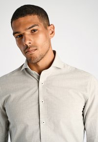 Hellgrau Button-up Hemd aus weichem Stoff, mit einem scharfen Kragen und subtiler Textur sowie dunklen Knopfakzenten.