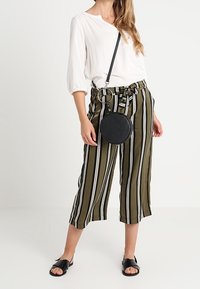 Culottes de color verde olivo a rayas con rayas blancas y negras, combinados con una blusa blanca. Un bolso cruzado negro y sandalias planas negras.