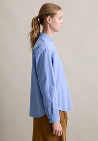 Lichtblauw katoenen shirt met een mandarinenkraag, lange mouwen en zijsplitten aan de onderrand, gecombineerd met bruine ribfluweel broek.