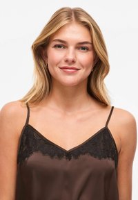 Camisole en satin marron avec bordure en dentelle noire le long du décolleté, dotée de fines bretelles réglables et d'une texture lisse.
