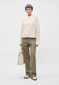 Κρεμ πλεγμένο καρντάν με κουμπιά, ελαιόχρωμο παντελόνι σε φαρδιά γραμμή, κρεμ τσάντα και ανοιχτόχρωπα παπούτσια με τρυπήματα. Απλός, καθαρός σχεδιασμός.