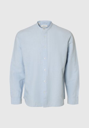 Gaiši zila lina krekls ar garām piedurknēm, mandarīnu apkakli un baltām pogām priekšpusē vienkāršā fonā.