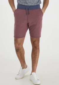 Burgundske sweat kratke hlače s tamnoplavim elastičnim pojasom, uže za podešavanje i bočnim džepovima. Tkanina je teksturirani pamuk.
