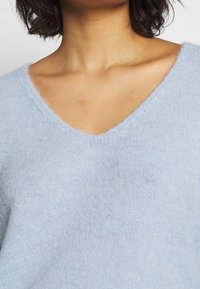 Jasnoniebieski, miękki, puszysty sweter z dekoltem w serek. Charakteryzuje się luźnym krojem i dzianą teksturą. Brak widocznych wzorów lub okucia.