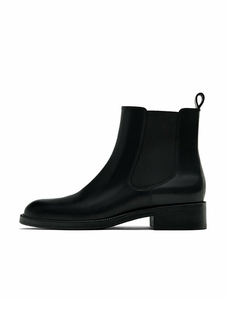 Bottine Chelsea en cuir noir avec panneaux latéraux élastiques, petit talon et languette à l'arrière sur fond blanc.