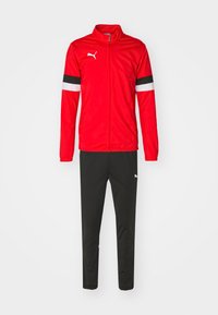 Rød sportsjakke med høy krage, svarte og hvite striper på ermene, kombinert med svarte bukser med en liten logo på låret.