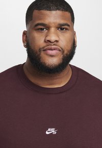 Sweatshirt Nike SB bordeaux com decote redondo e logótipo branco no peito. Textura lisa e mangas curtas, focado na parte superior do corpo.