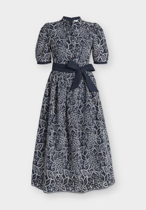 Μίντι φόρεμα σε ναυτικό μπλε με λευκό περίτεχνο μοτίβο φύλλων, φουσκωτά κοντά μανίκια, ψηλό λαιμό και ζώνη από το ίδιο ύφασμα δεμένη στη μέση.