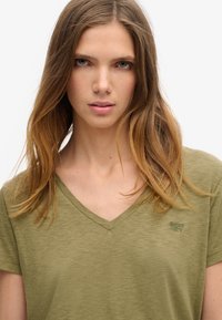 Olivengrøn V-hals t-shirt lavet af letvægtigt stof, med korte ærmer og et diskret logo broderet på brystet.