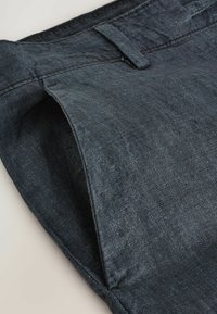 Pantalon en denim bleu foncé avec une texture lisse et un subtil éclat. Les caractéristiques incluent une coupe droite, des passants de ceinture et des poches latérales.
