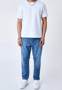 Camiseta blanca de algodón con un bordado sutil, combinada con jeans de mezclilla azul claro que presentan un patrón geométrico, complementada por unas zapatillas blancas.