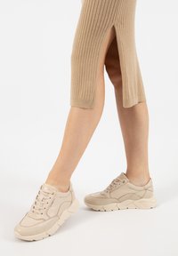 Sneaker beige con tomaia in pelle texturizzata, chiusura a lacci, collo imbottito e suola in gomma spessa. Abito midi beige a costine con spacco laterale.