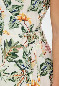 Vestido envolvente floral con hojas verdes, flores naranjas y amarillas, y un cierre de lazo en la cintura sobre un fondo claro. Textura de tela suave.