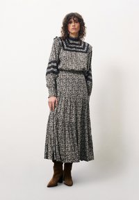 Zwart-wit jurk met een bloemmotief, lange mouwen, ruches op de taille en zwarte gestreepte accenten; gecombineerd met bruin leren laarzen met hak.