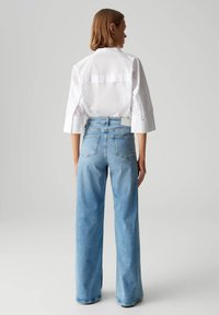 Jean large bleu clair à taille haute avec des poches arrière, associé à une chemise blanche à col avec des manches trois-quarts.