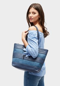 Blauwe draagtas van textuurleer met denimstrepen, met een donkerblauwe basis. Comfortabele schouderbanden voor gemakkelijk dragen.