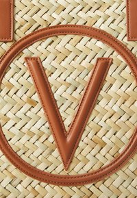 Vävd halmvecka med ett stort brunt läder "V" och cirkulär läderkant, i en naturlig tanfärg och med en strukturerad yta.