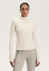 Lightweight, cream-colored puffer jacket with a zip closure and panel detailing, featuring long, fitted sleeves and smooth fabric texture.