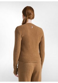 Brauner Rippstrickpullover mit langen Ärmeln, figurbetontem Design und einem kleinen Etikett am Hinterkragen. Weiche Textur und nahtlose Verarbeitung.