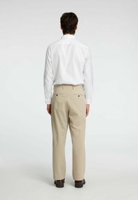 Biała koszula z długim rękawem i beżowe spodni w paski, z tylnymi kieszeniami i prostym krojem, noszone z ciemnymi butami, widok z tyłu.