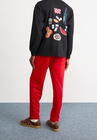 Svart långärmad tröja med färgglada mat- och drycksgrafik på baksidan. Röda träningsbyxor, bruna sneakers med gummisula.