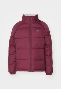 Giacca imbottita borgogna con colletto alto, chiusura con zip e tasche laterali; presenta una patch con logo sul petto e polsini a costine.