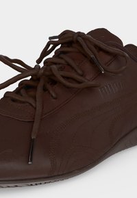 Κοντινή λήψη ενός καφέ δερμάτινου αθλητικού παπουτσιού Puma με καφέ κορδόνια δεμένα σε φιόγκο και ραφές στη πλευρά.