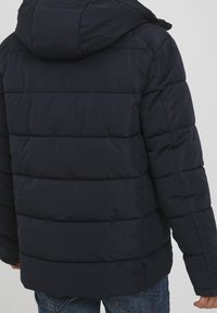 Dunkelblaues Steppjacke mit horizontalen gesteppten Abschnitten, einer Kapuze und einer glatten Außenseite. Weiche Textur; geeignet für kaltes Wetter.