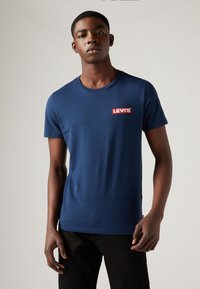 Tricou din bumbac de culoare bleu marin, cu guler rotund și mâneci scurte, având un patch cu logo-ul roșu Levi's pe piept. Textură simplă, design ajustat.
