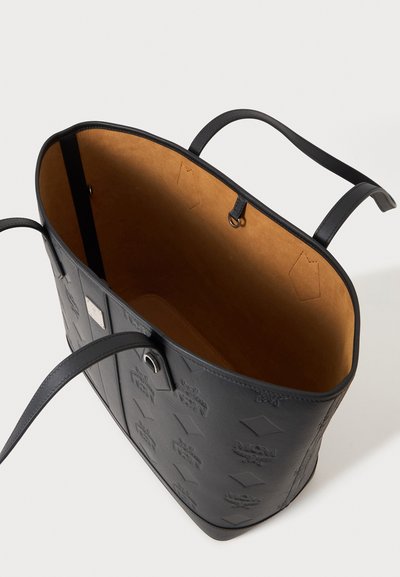 Sac cabas en cuir noir avec motif embossé et intérieur couleur beige, doté de deux poignées avec un dessus ouvert.